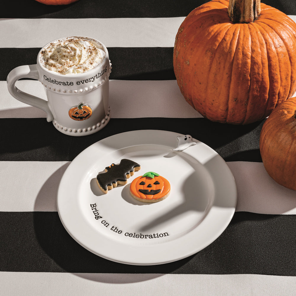 Halloween mug with whipped cream and pumpkin cookies on a "Bring on the celebration" plate with real pumpkins.