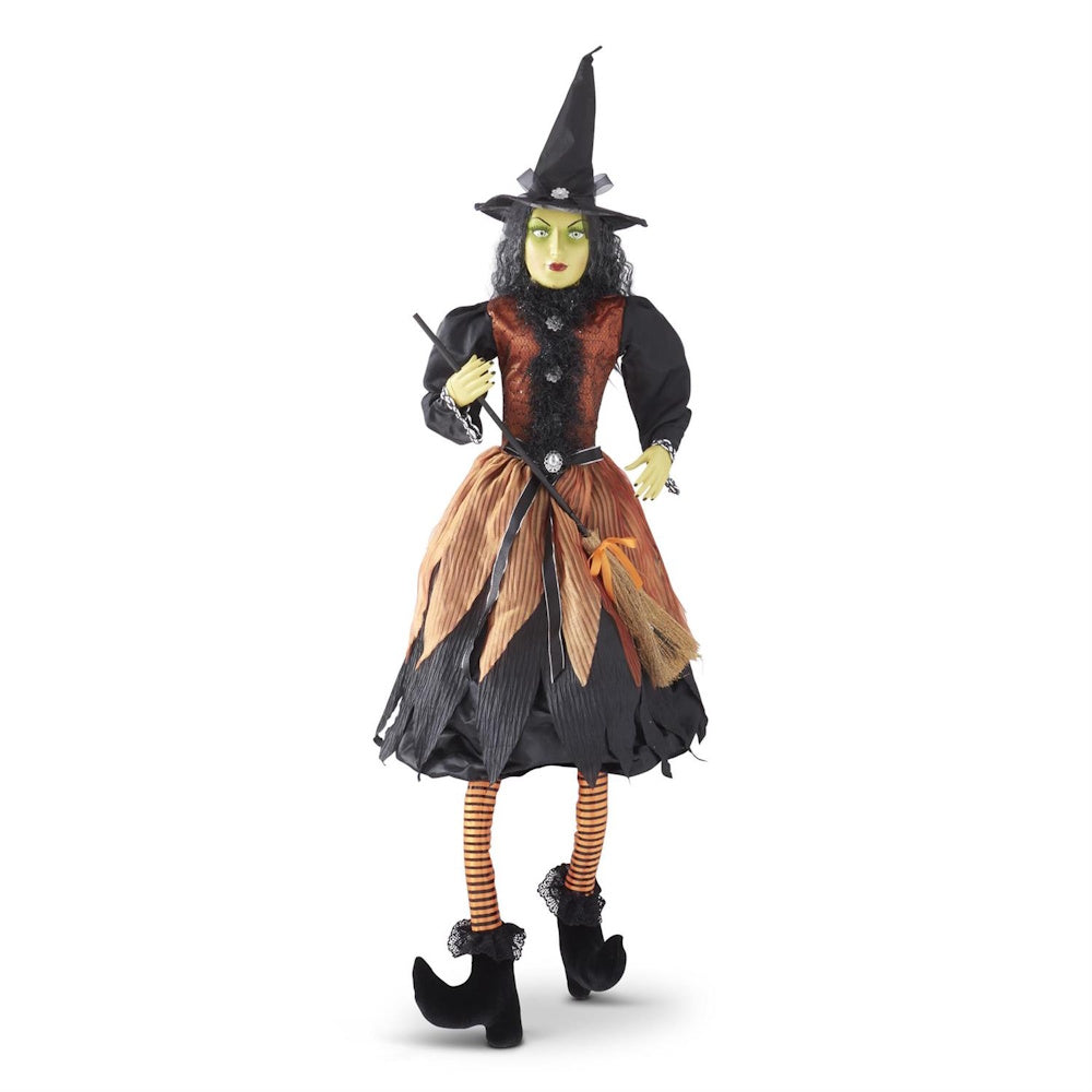 Green-skinned witch figurine wearing a pointed black hat, orange dress, and holding a broom.