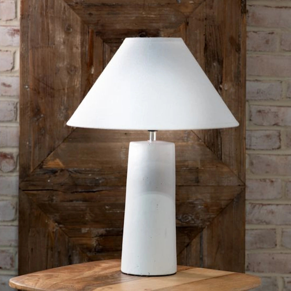 Minimalist white ceramic table lamp with tapered base and white conical shade on a wooden table.