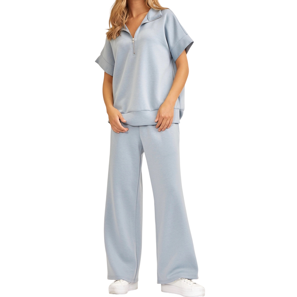 A woman wears a light slate blue lounge set featuring a short-sleeve quarter-zip top and wide-leg pants.