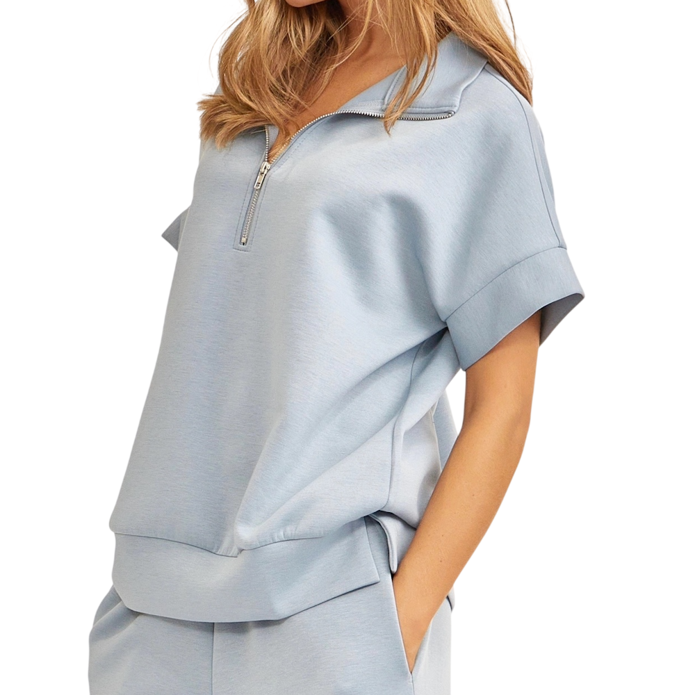 A close-up of a woman wearing a light slate blue short-sleeve quarter-zip pullover with matching pants.