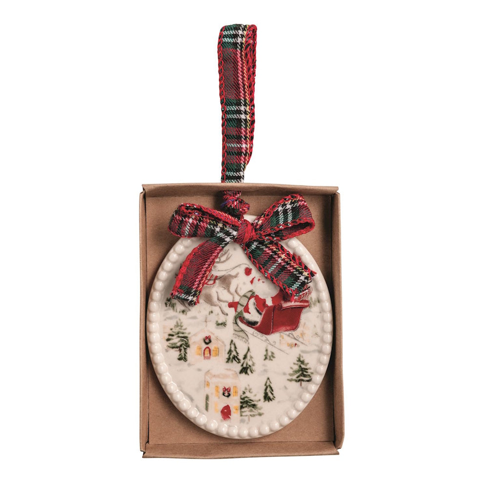 Oval ceramic ornament showing Santa in his sleigh over a snowy town, with plaid bow and ribbon.