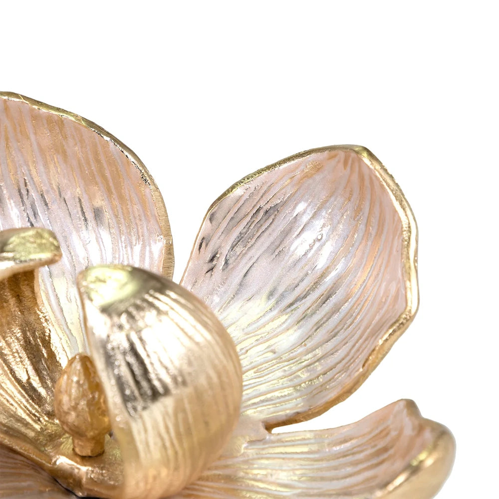Close-up of a small, elegant gold and pale pink enamel flower sculpture with detailed petals against a white background.