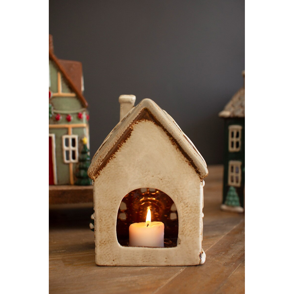 Back view of a ceramic Christmas village house showing a lit tea light candle inside.