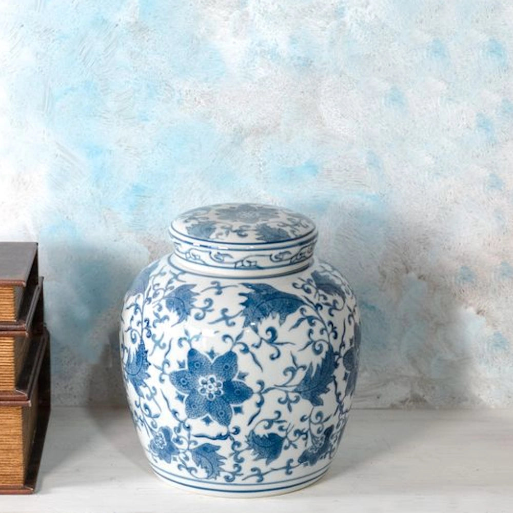 Blue and white floral porcelain ginger jar with lid on a white shelf next to vintage books and a blue textured wall.
