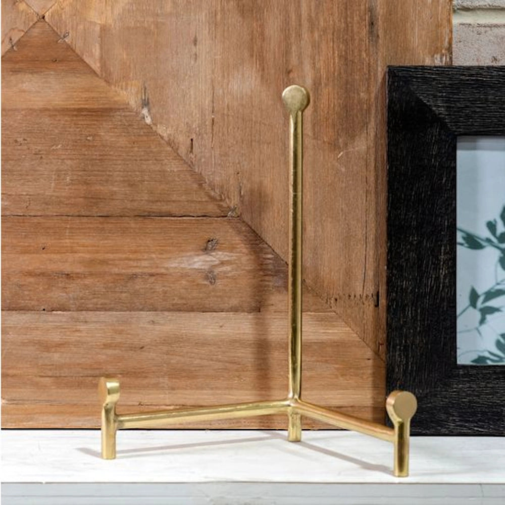 Small brass straight-back easel stand for displaying photo frames or art, shown against a rustic wood background.