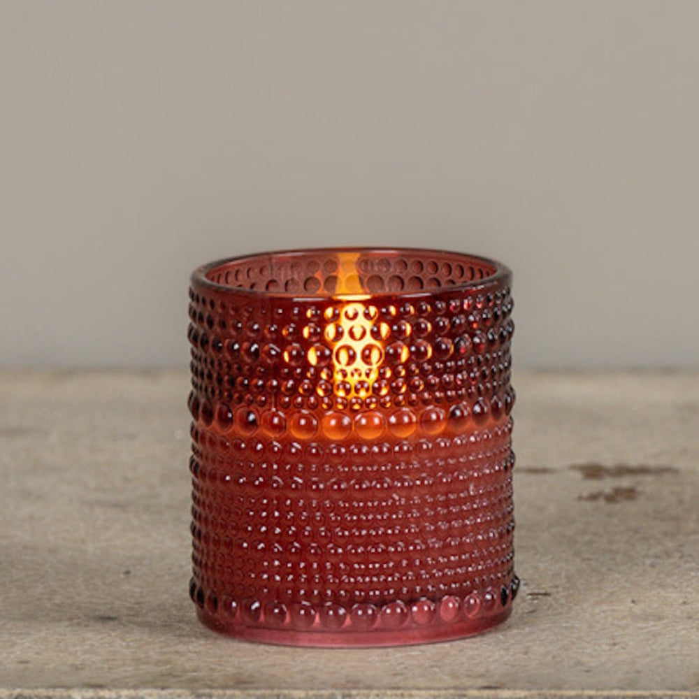 Lit burgundy beaded glass candle holder sitting on a wooden surface.