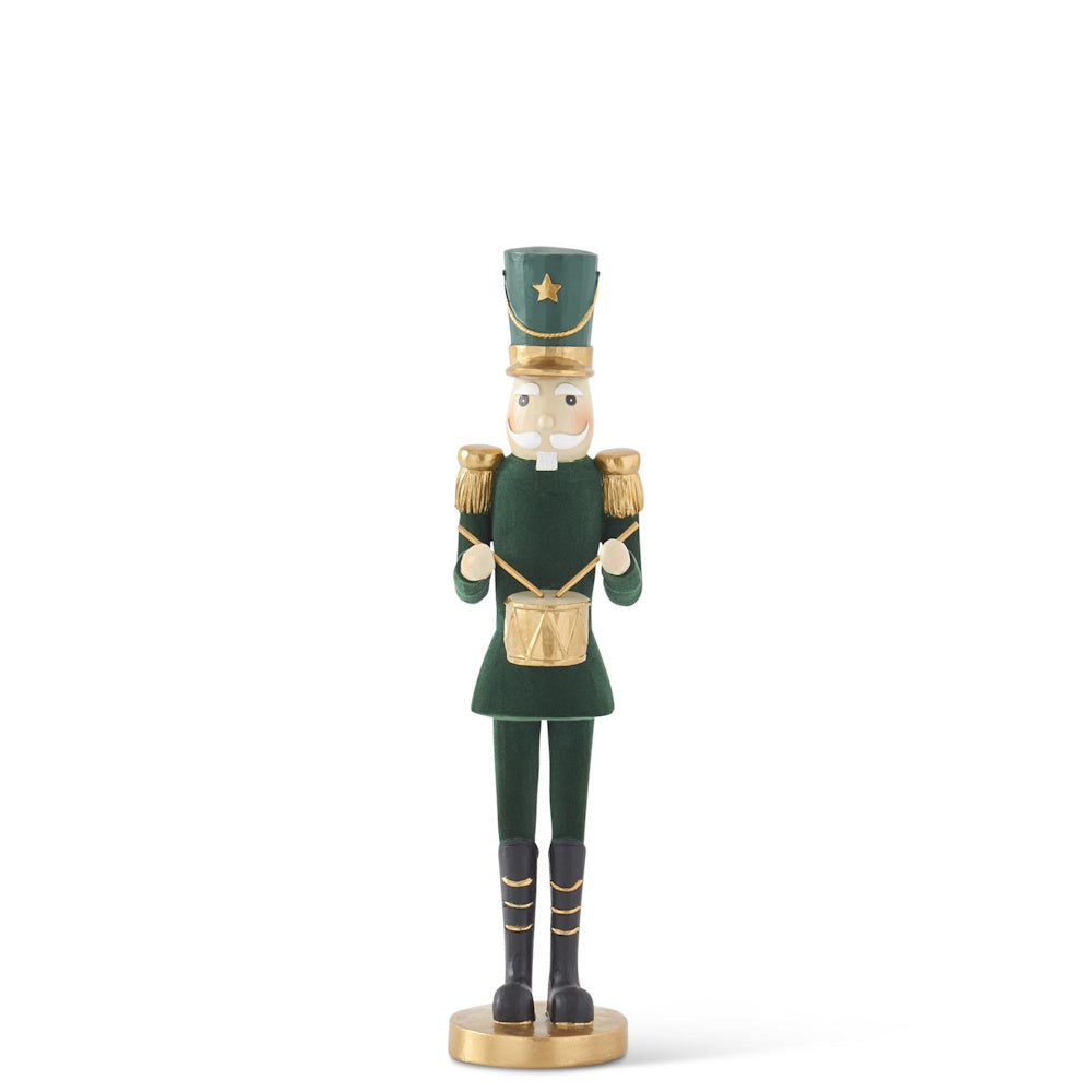 A dark green velvet nutcracker figurine in a gold-trimmed uniform playing a small drum against a white background.