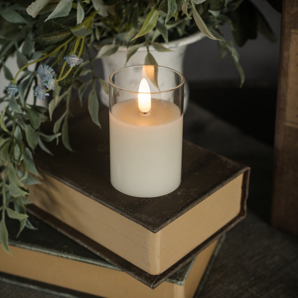 Small glass flameless pillar candle glowing on a stack of vintage books next to greenery.