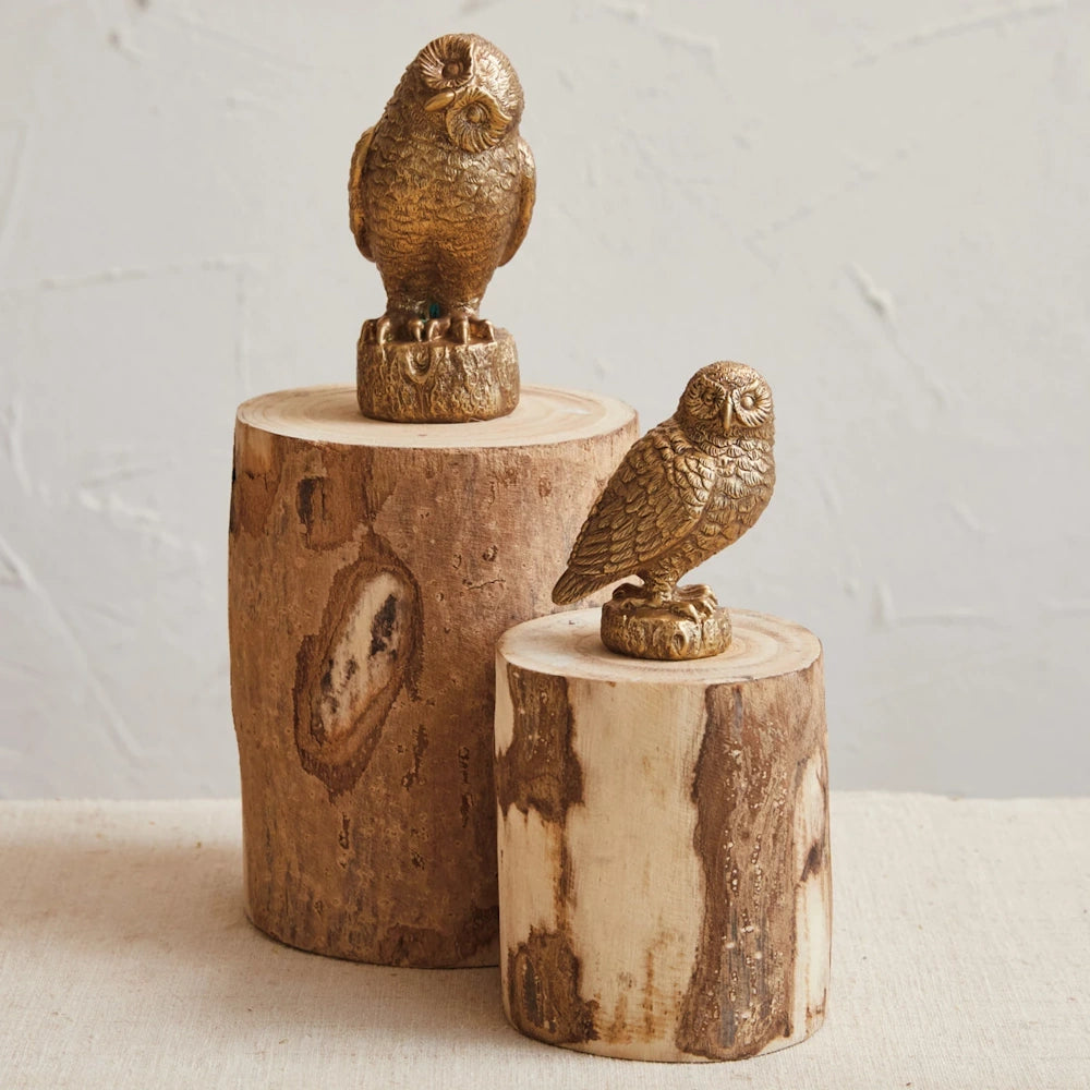 Two small, gold-finished resin owl figurines perched on rustic wooden log pedestals.