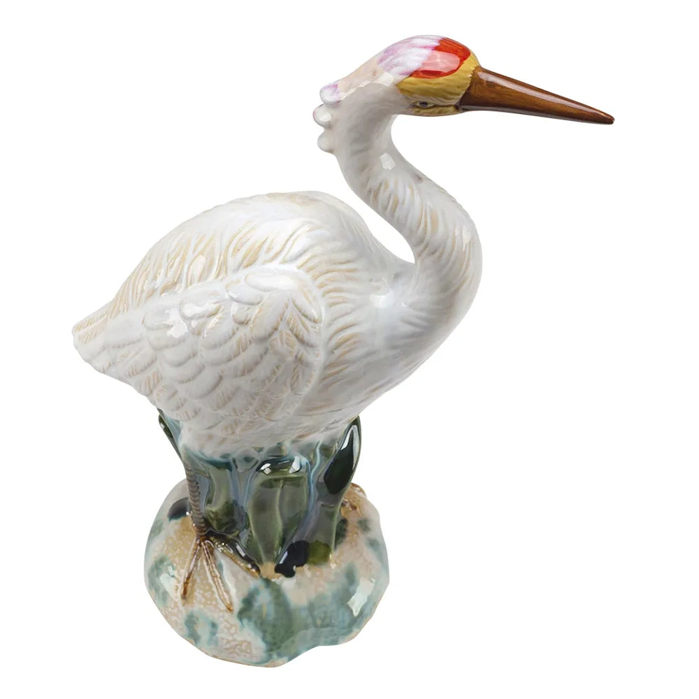 A ceramic figurine of a white heron with a red and yellow crown patch, standing on a green and blue base.