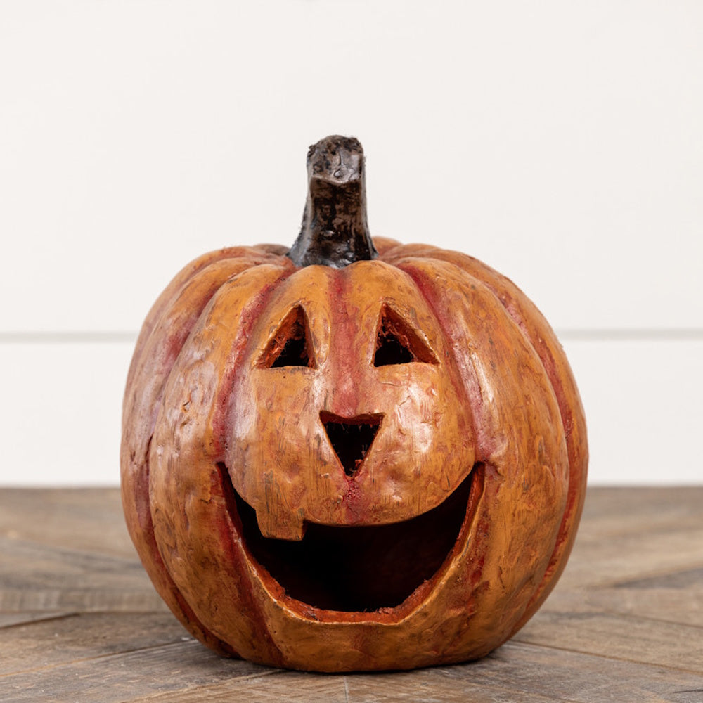 Carved rustic orange jack-o'-lantern with a wide smiling mouth sitting on a wooden surface.