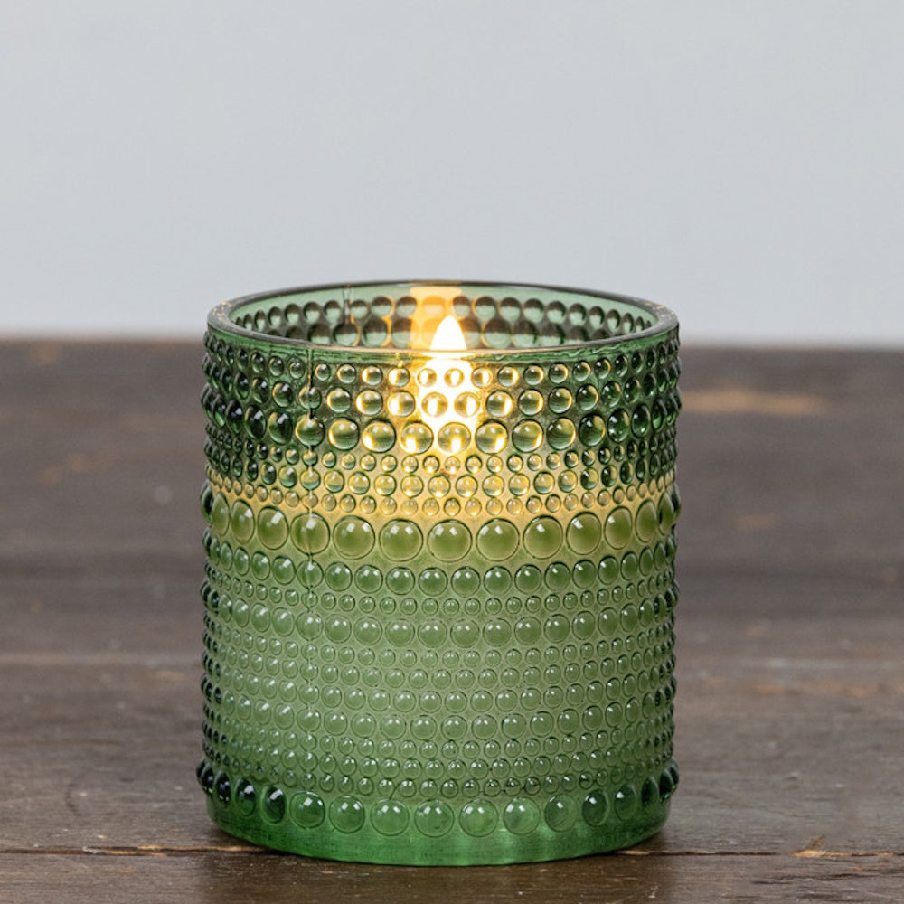 Small green hobnail glass candle holder with a glowing flame inside, sitting on a wooden surface.