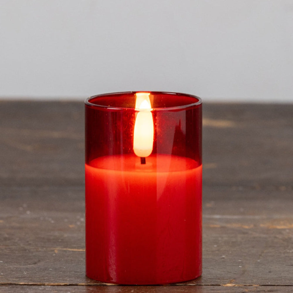 A small red glass flameless candle glowing bright on a dark wooden surface.
