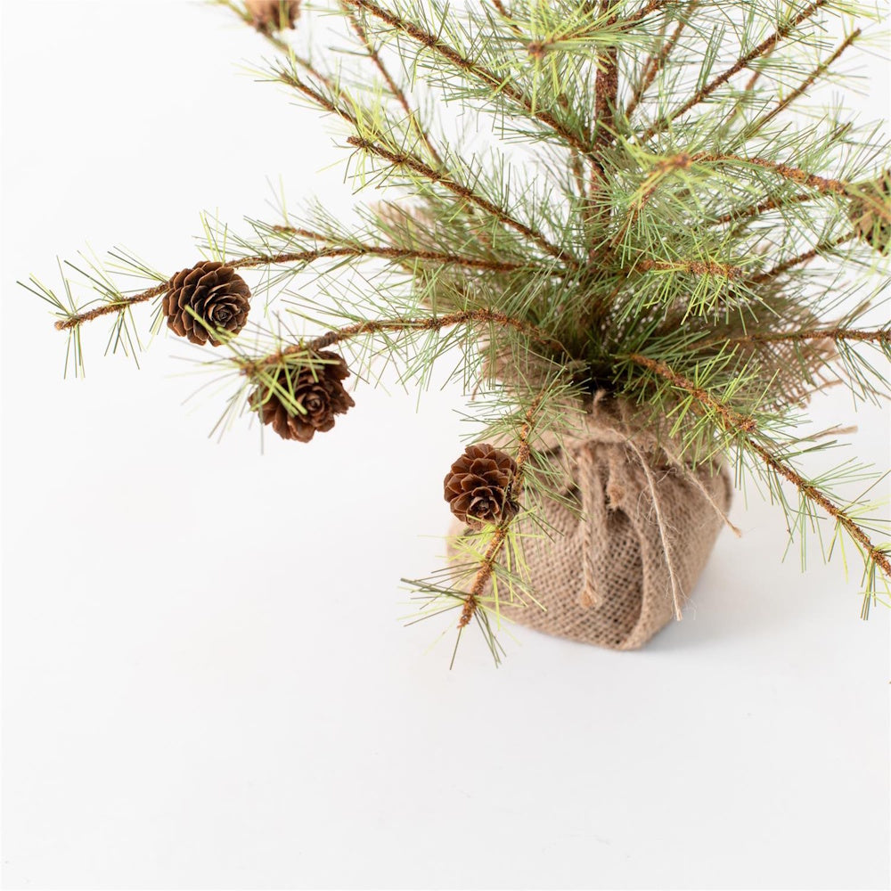 This is a miniature artificial pine tree decorated with small pinecones, featuring a base wrapped in rustic burlap tied with jute twine.