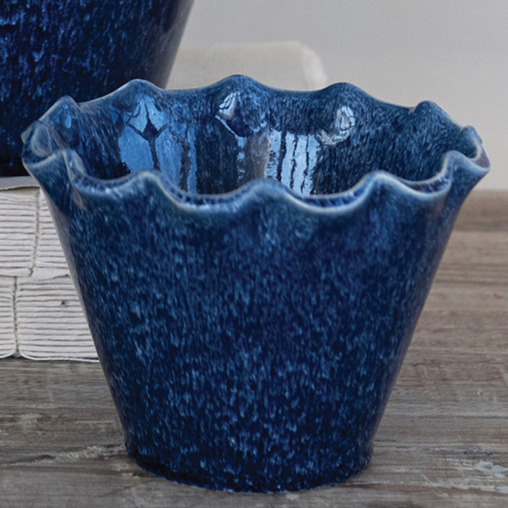 Small blue stoneware planter with a ruffled edge and speckled glaze, sitting on a rustic wooden surface.
