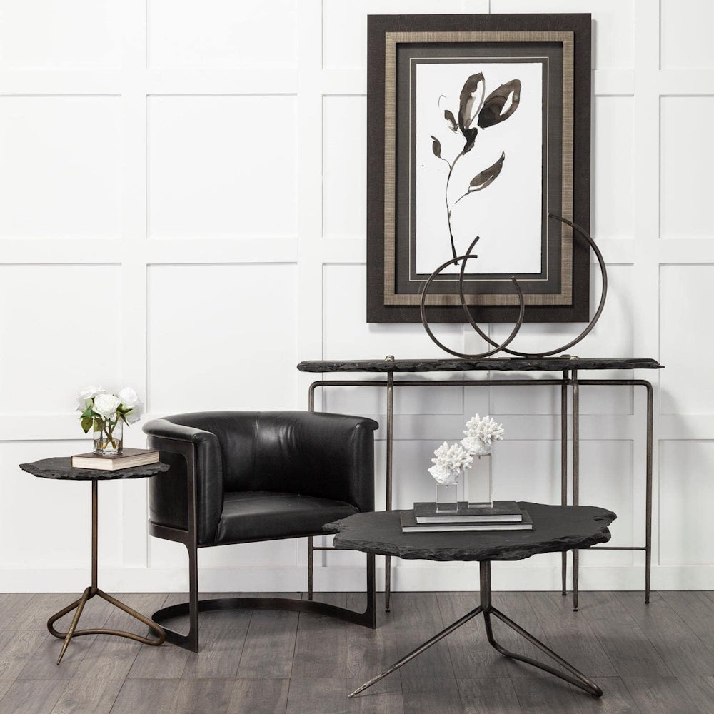 Modern black living room furniture set with stone tables, leather chair, and minimalist wall art in a white room.