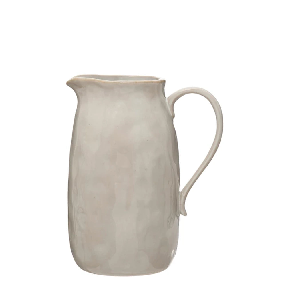 Rustic cream ceramic pitcher with hammered texture and handle on white background.