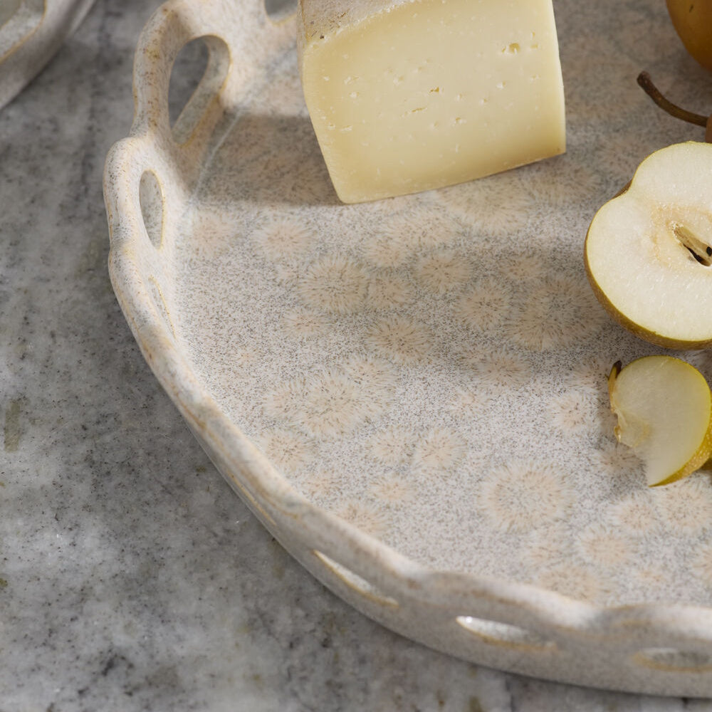 A ceramic tray with a scalloped edge holding cheese and cut pears on a marble surface.