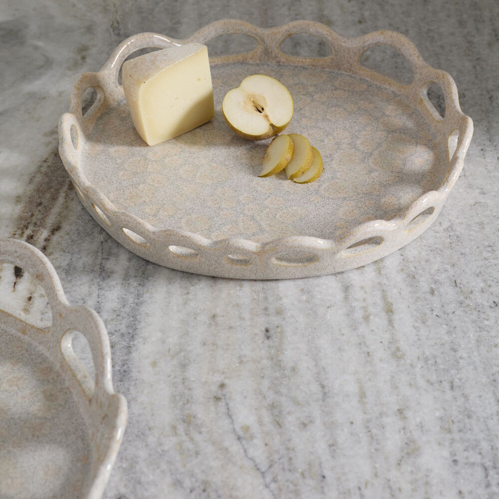 A ceramic speckled tray with a scalloped edge holding a wedge of cheese and a sliced pear on a marble surface.