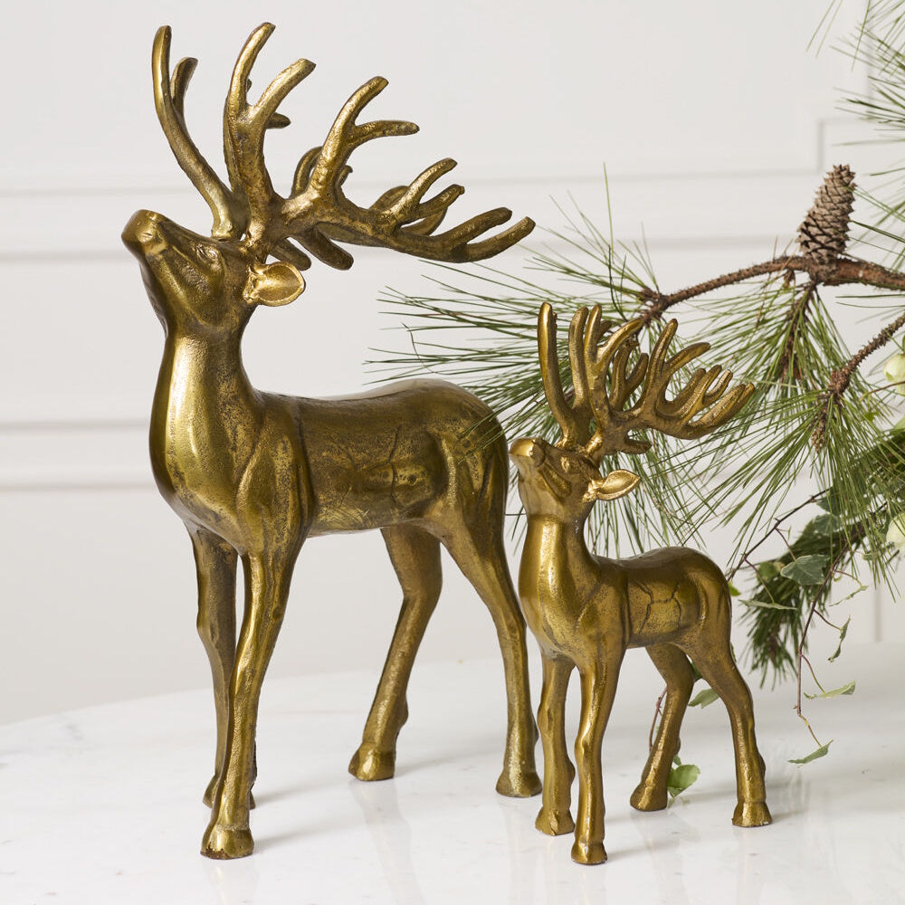 Two gold reindeer figurines of different sizes standing together next to pine branches.