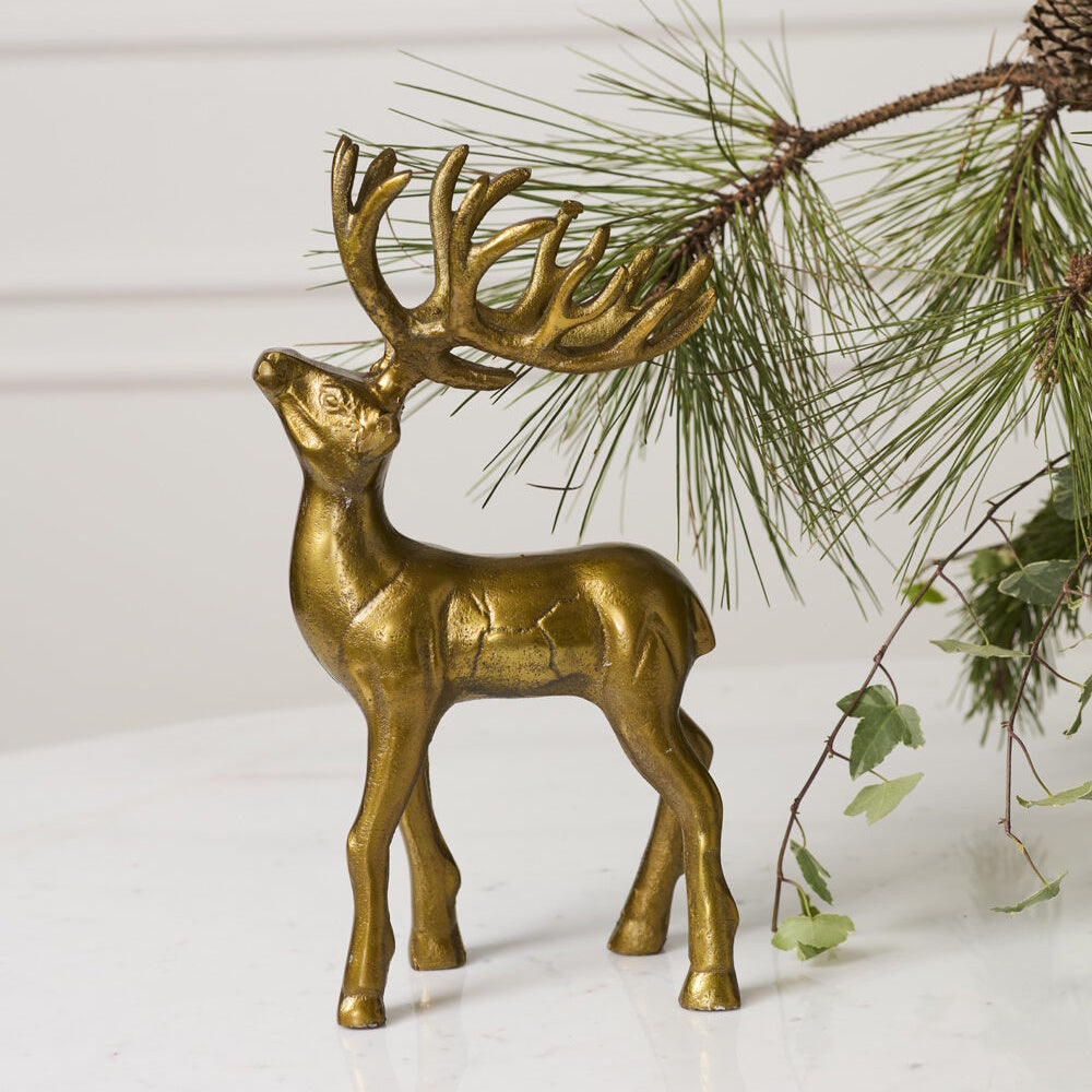 Gold reindeer figurine displayed on a marble surface next to pine branches.