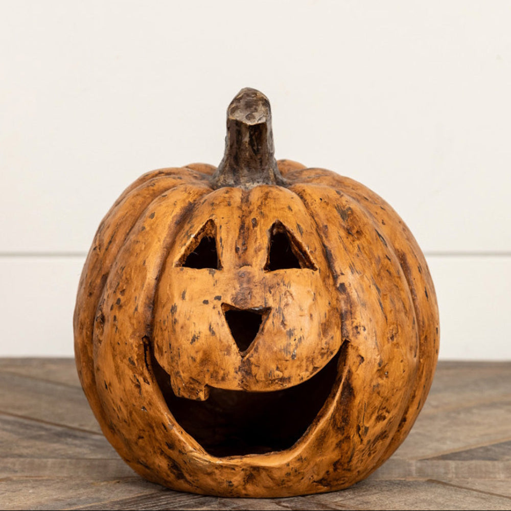 Small carved terracotta jack-o'-lantern sitting on a wooden surface against a white wall.