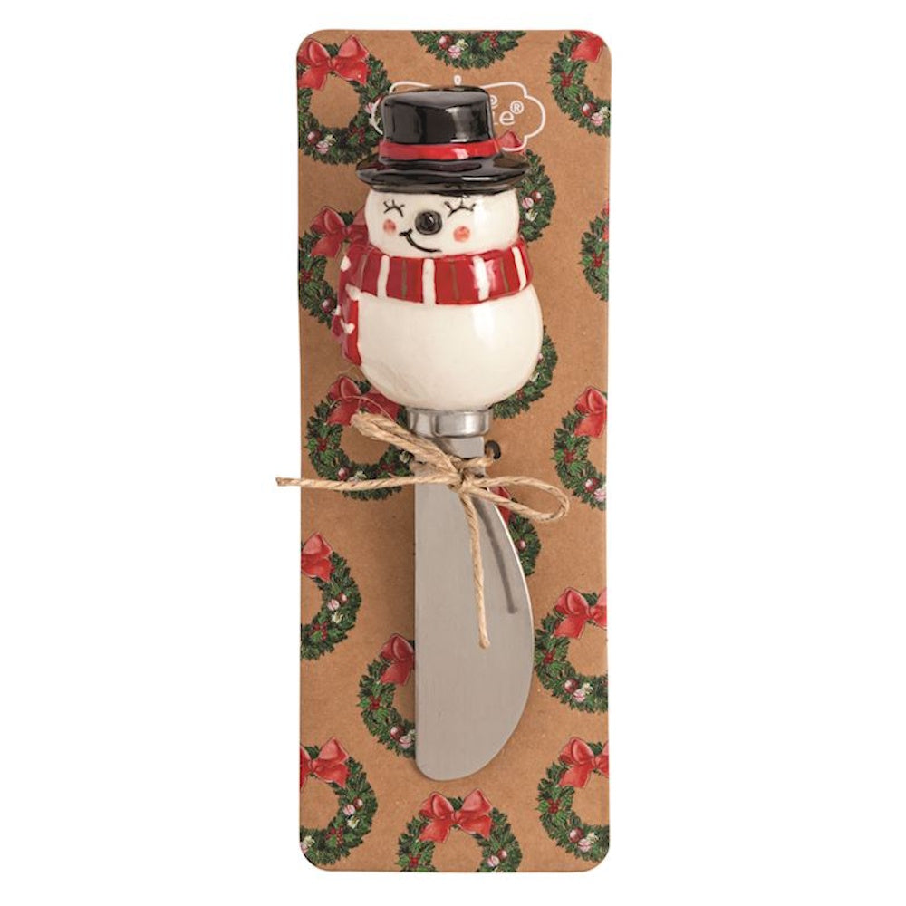 Cheese spreader with a ceramic snowman head handle on a wreath-patterned backing card.