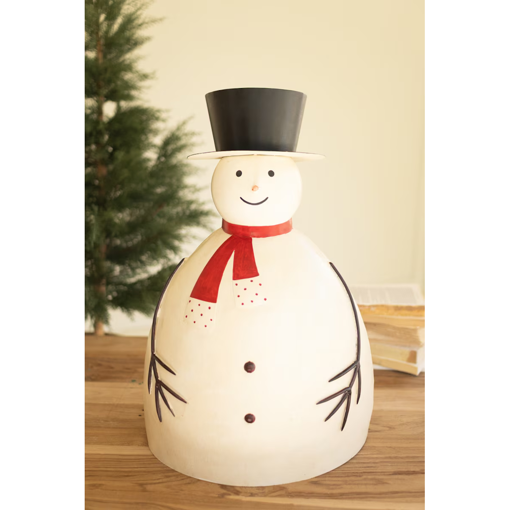 Large painted metal snowman sculpture placed on a wooden table beside Christmas greenery.