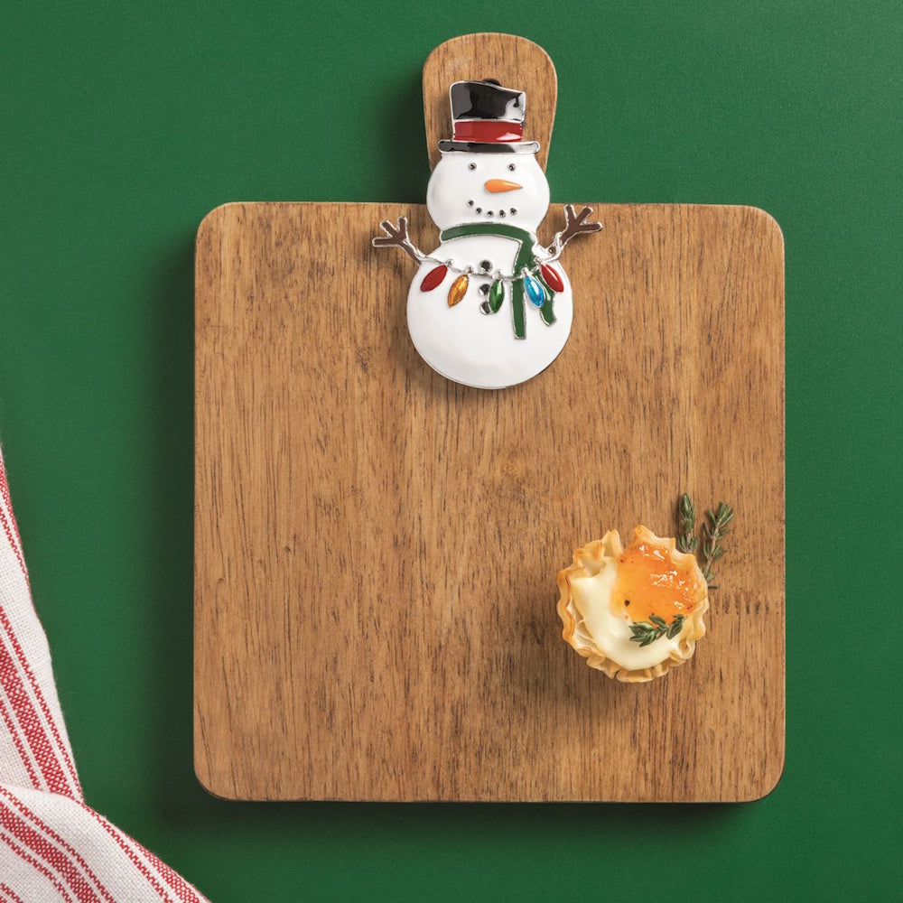 Mud Pie snowman interchangeable charm attached to a wooden charcuterie board with a holiday appetizer.