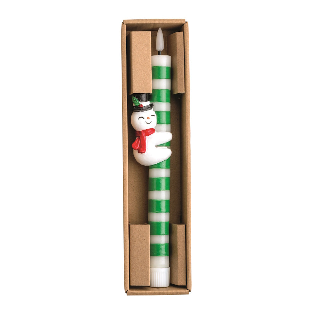 Top-down view of a green and white striped wax taper candle set in a cardboard box, featuring a snowman figurine hugging the candle shaft.