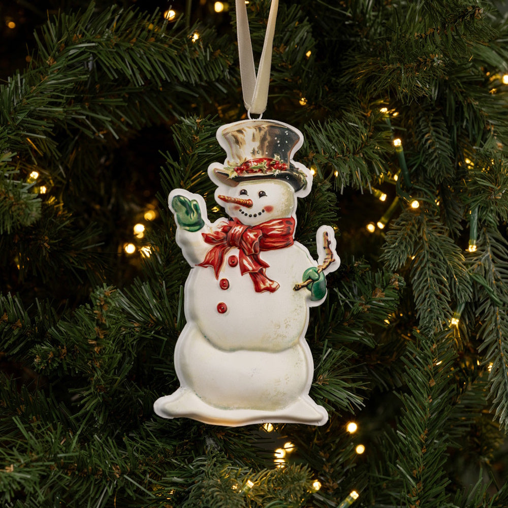 Vintage snowman ornament with top hat and red scarf hanging on a lit Christmas tree branch.
