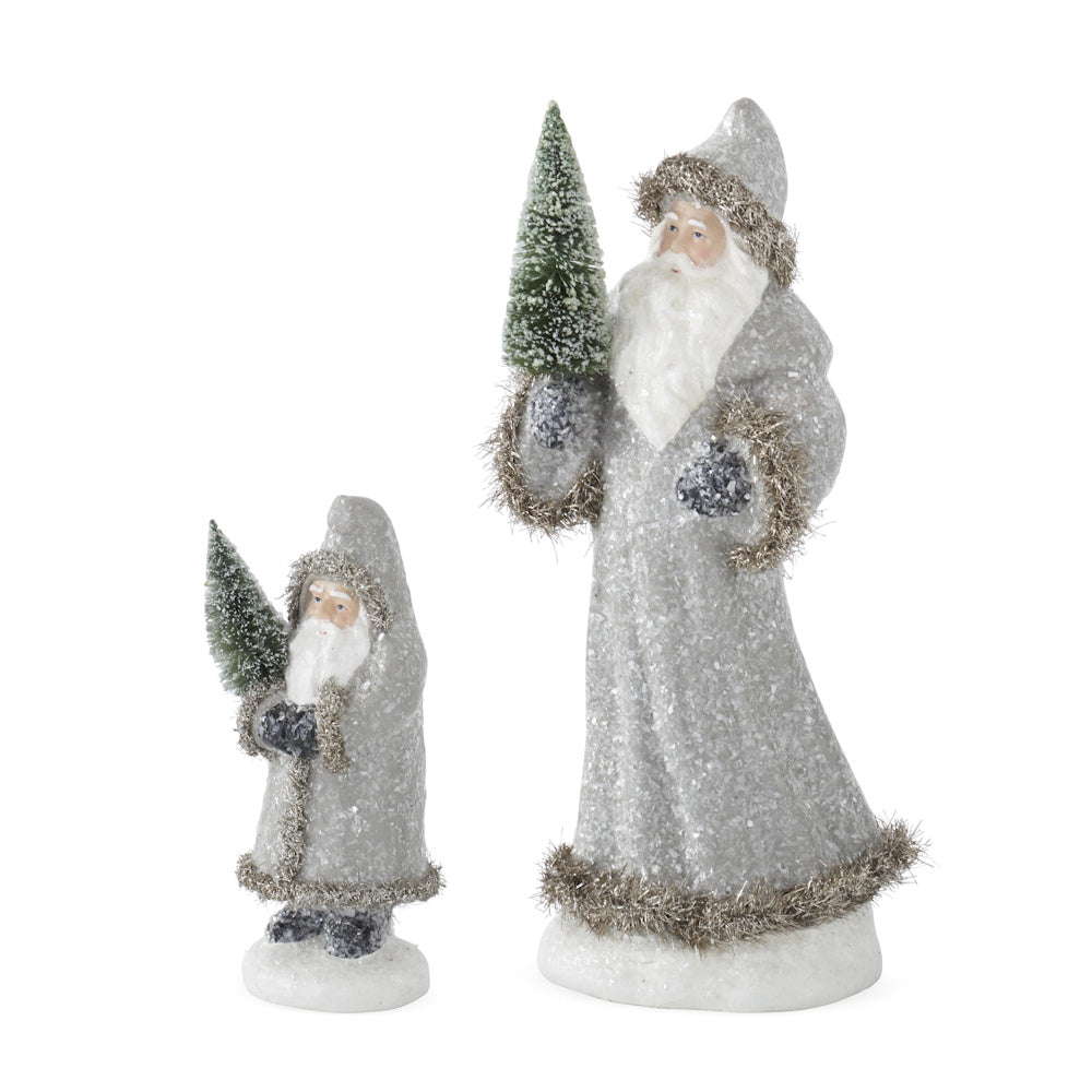Side view of 2 Santa figurines in snowy gray coats trimmed with tinsel, holding bottle brush trees.