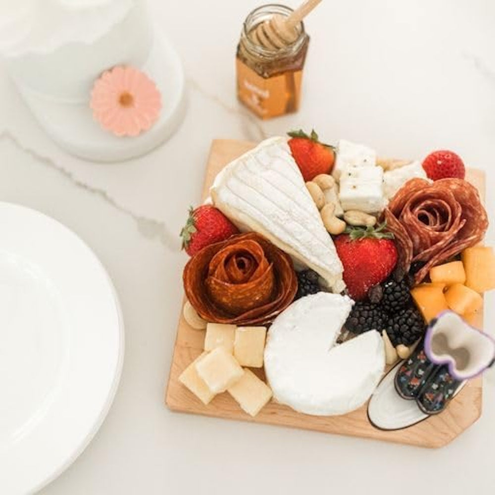 A mini charcuterie board with brie, salami roses, strawberries, and cheese cubes next to a jar of honey.