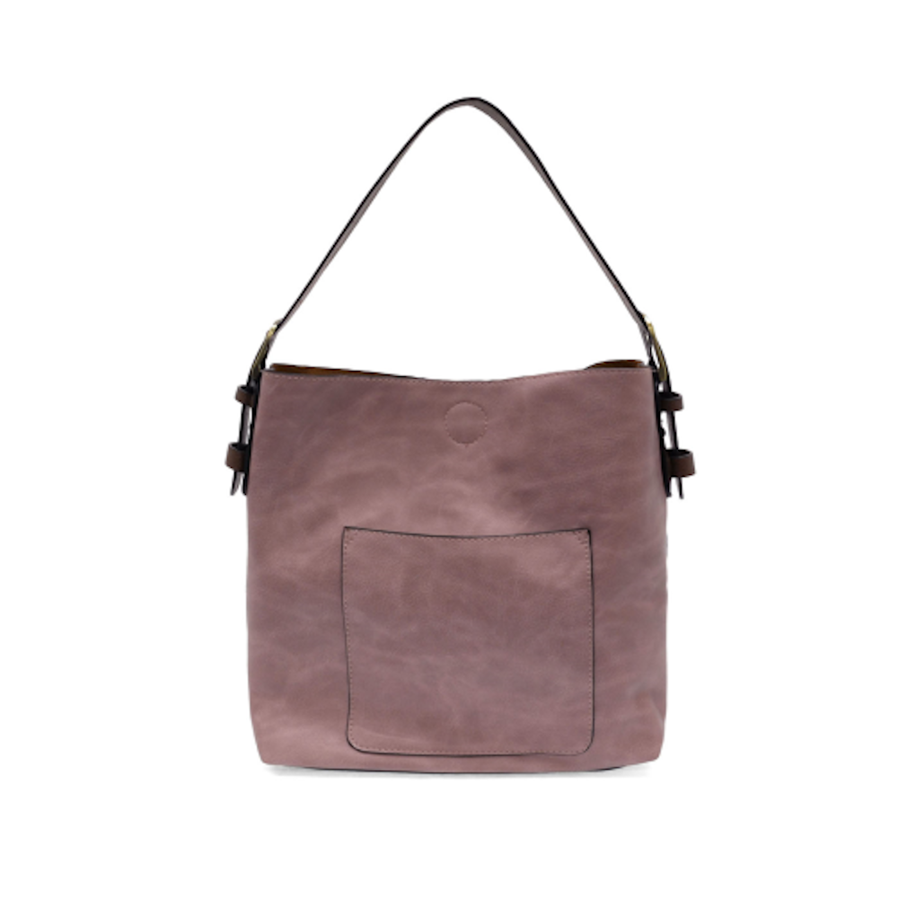 A dusty mauve faux suede hobo handbag with a brown handle and front pocket, on a white background.