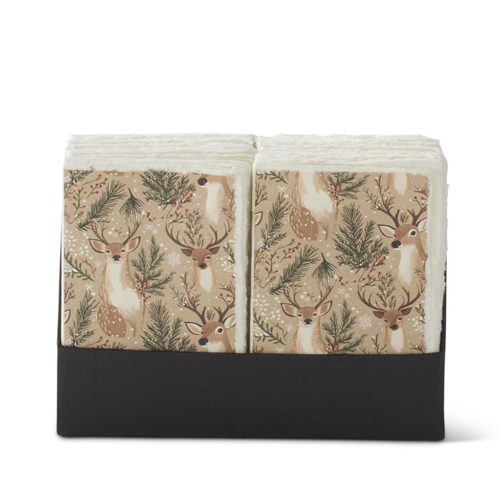 Stacks of holiday reindeer and pine napkins in a black holder.