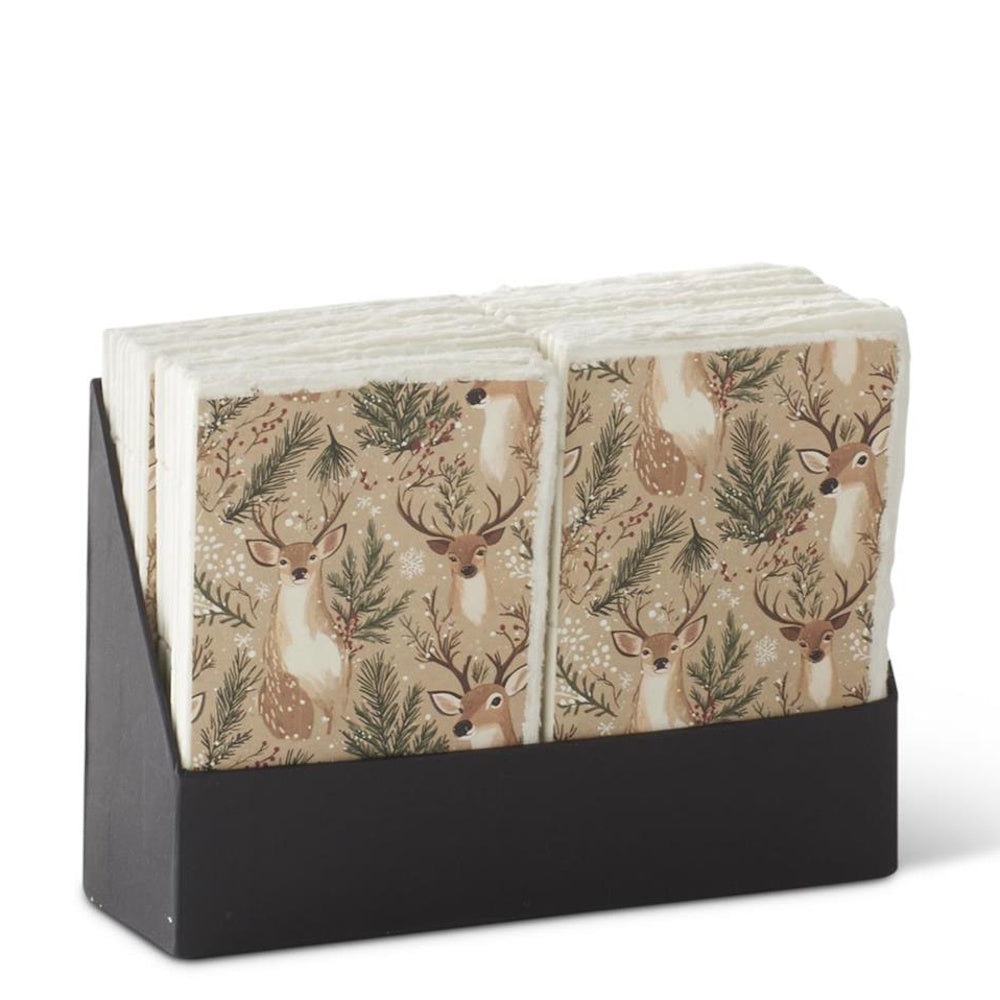 Stacks of decorative paper napkins featuring a holiday reindeer and pine pattern inside a black holder.
