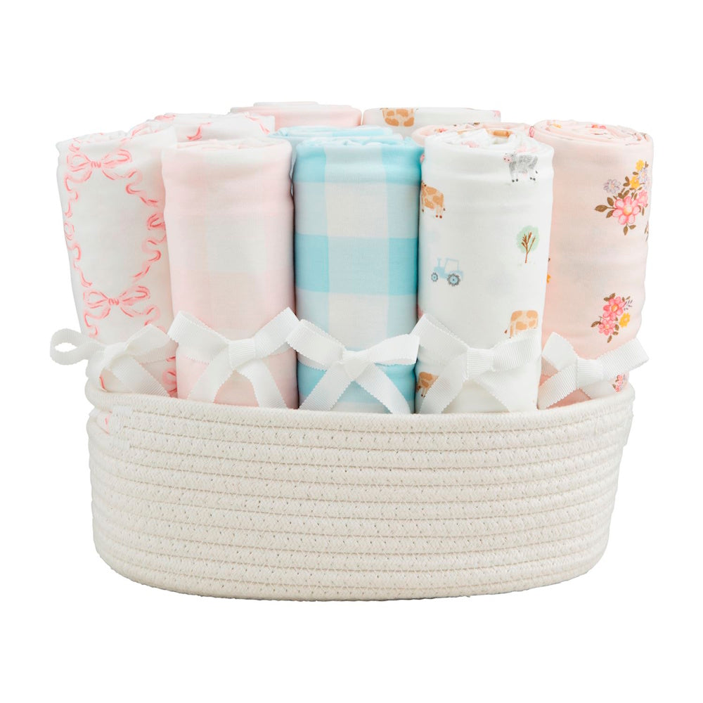 Assorted rolled soft knit baby swaddle blankets with bows in a white woven rope storage basket.