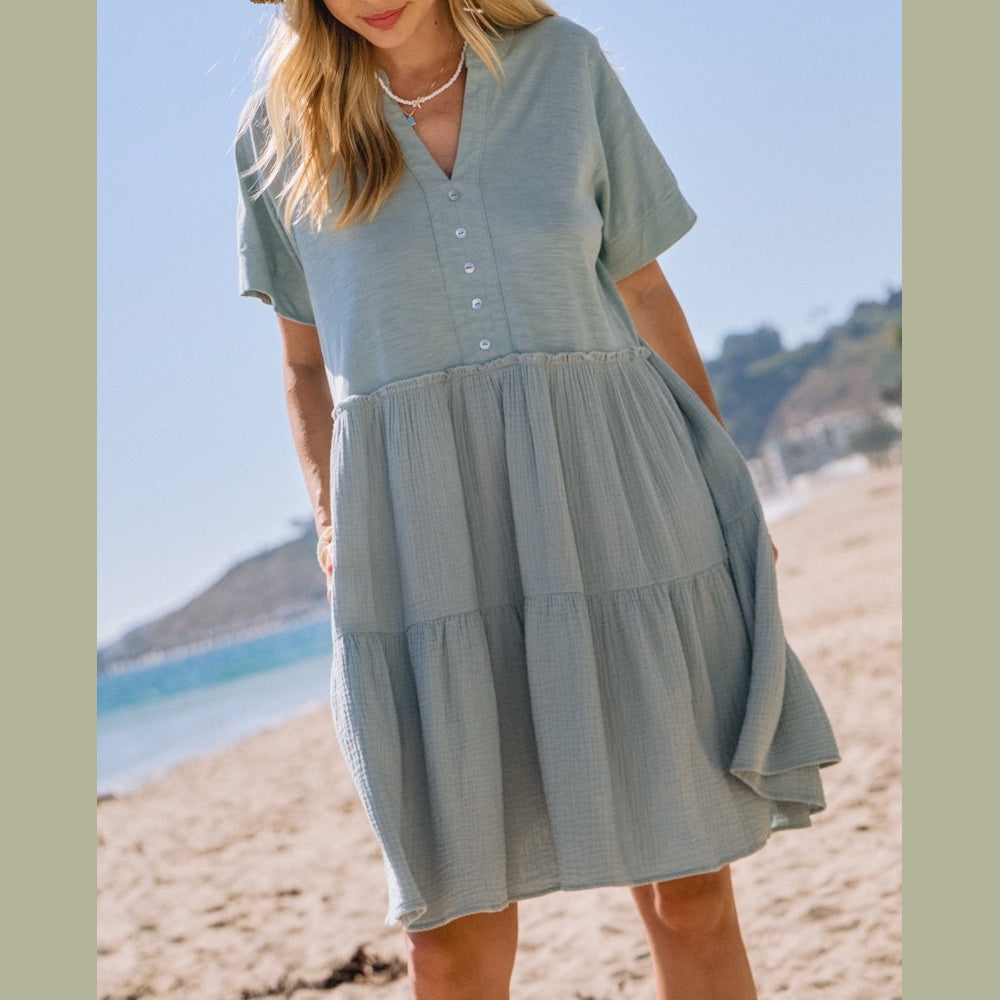 Woman wearing a light blue, tiered, short-sleeved cotton dress on a sunny beach.