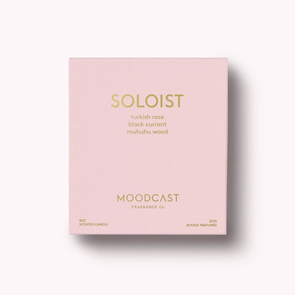 Soft pink Moodcast Soloist scented candle box with gold lettering on a light background.