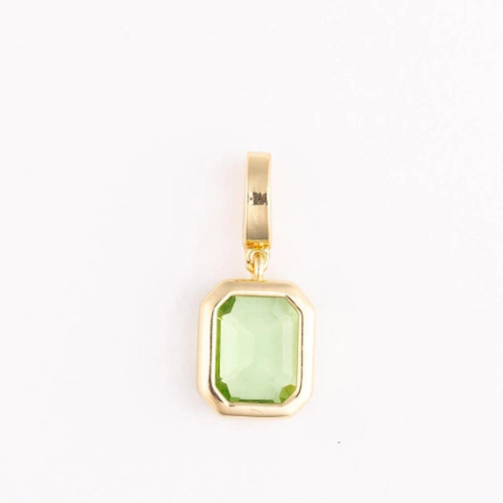 A polished gold pendant charm with an emerald-cut light green gemstone on a plain white background.