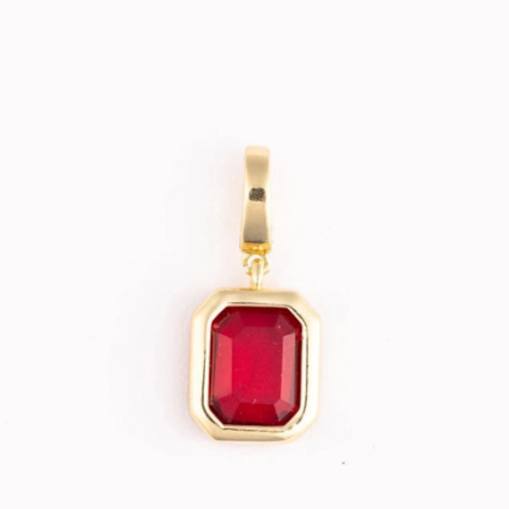 A polished gold pendant charm with an emerald-cut red gemstone on a plain white background.