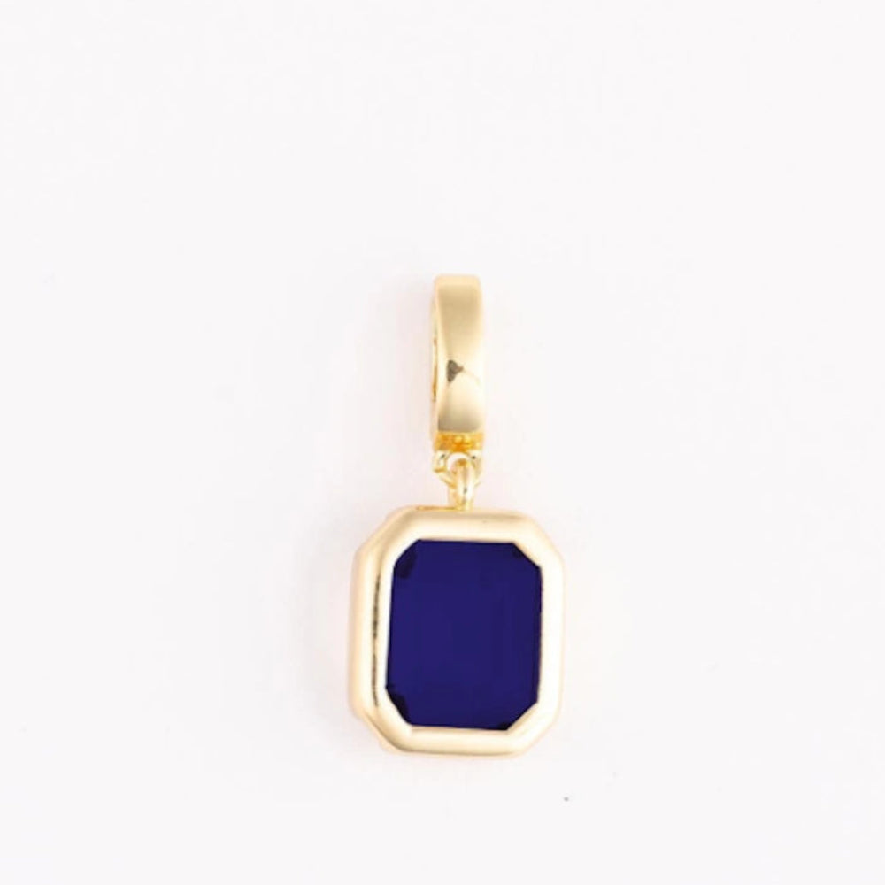 A polished gold pendant charm with an emerald-cut dark blue gemstone on a plain white background.