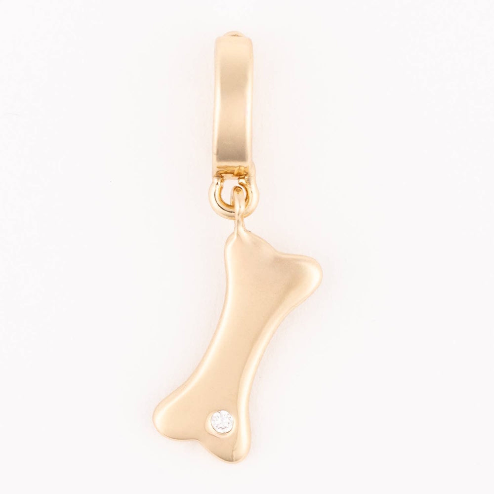 Gold dog bone charm pendant set with a small crystal on a white background.