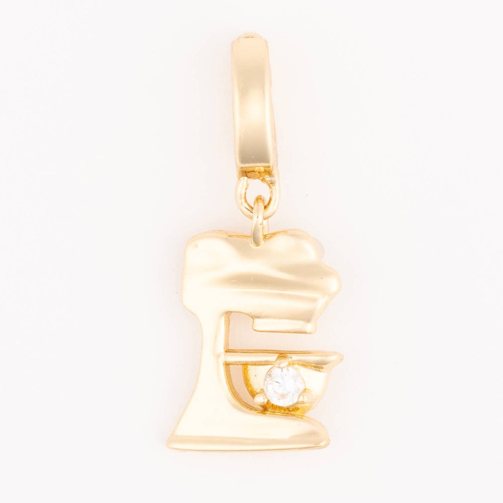 A polished gold pendant charm in the shape of a stand mixer with a small stone detail on a plain white background.