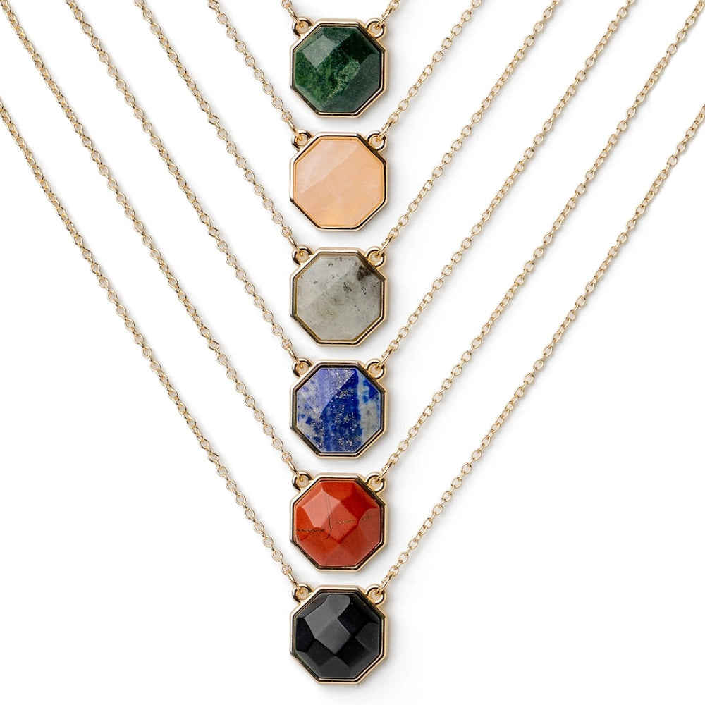 Six gold necklaces with hexagonal gemstone pendants in green, peach, grey, blue, red, and black on a white background.