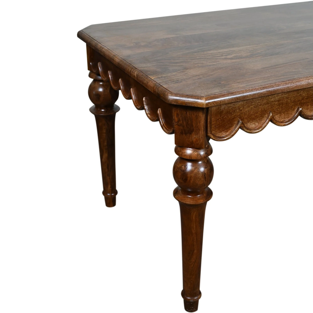 Dark wood dining table with scalloped apron and turned legs on white background.