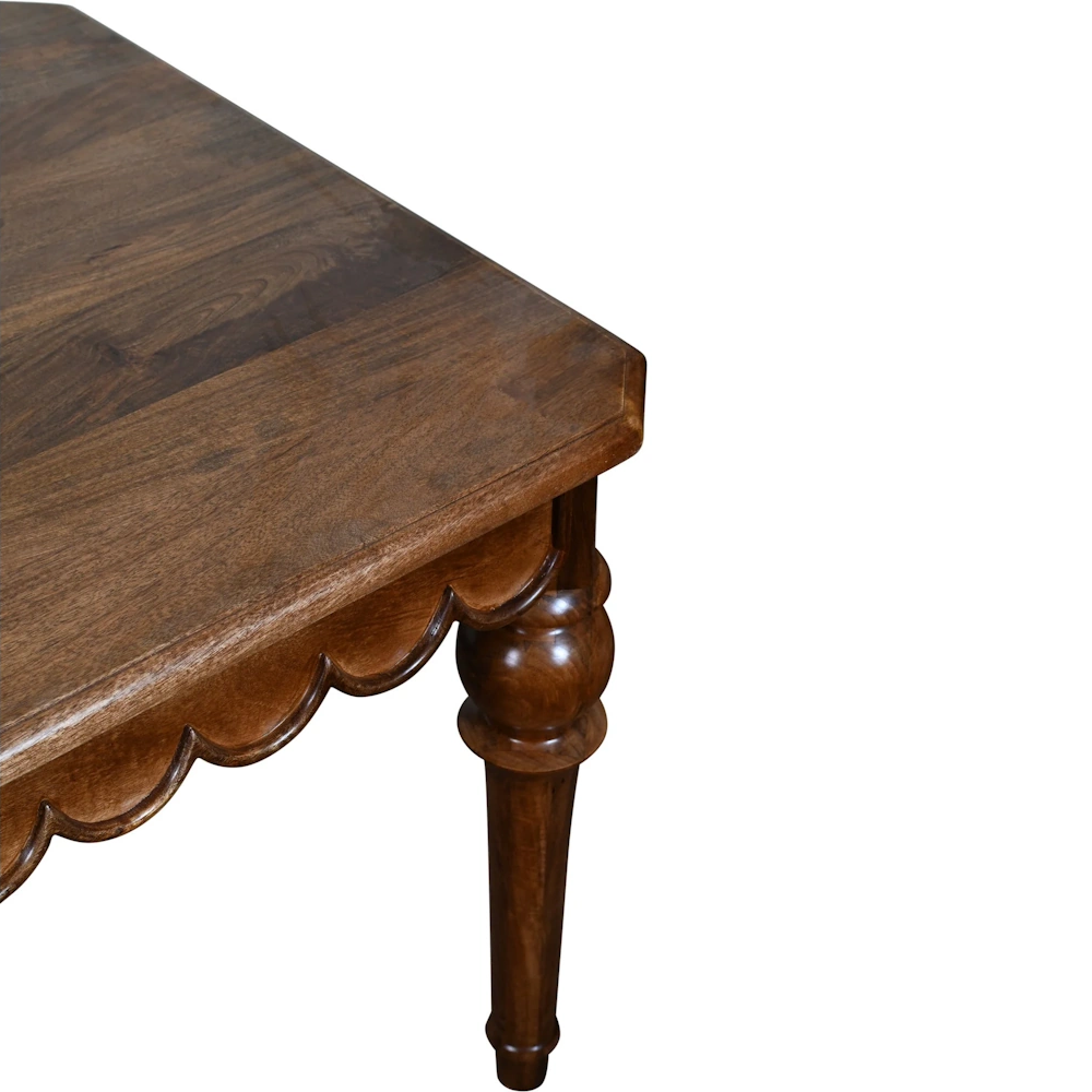 Close-up of a dark wood dining table featuring a scalloped apron and a carved, turned pedestal leg.