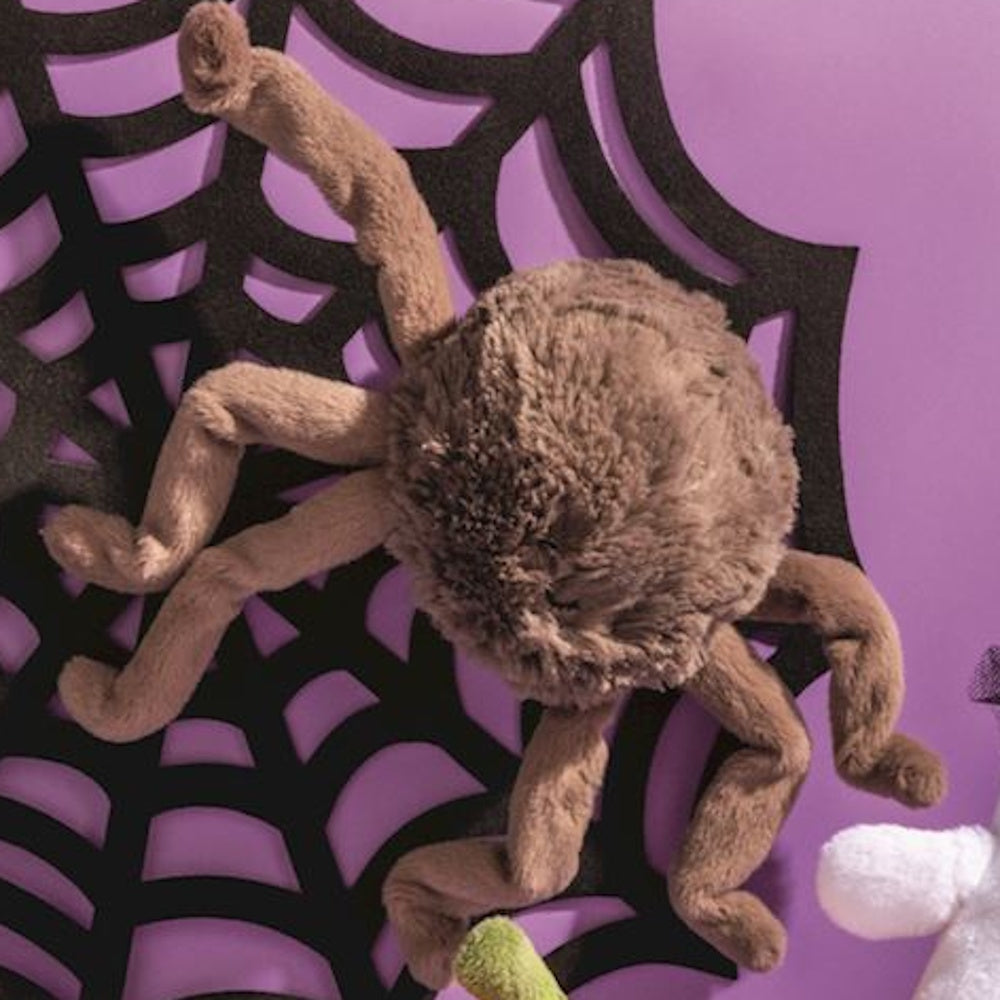 A fluffy, brown plush spider decoration attached to a large black spiderweb cut-out on a purple background.