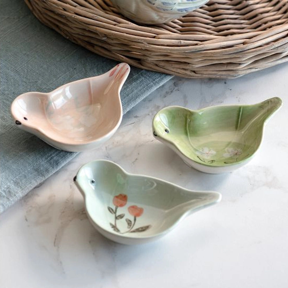 Three bird-shaped ceramic mini dishes in pastel pink and green with floral details on a white marble surface.